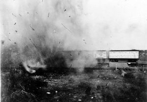 Pictured in black and white is flying debris from the train wreck at Crush. A few still unaffected train cars are seen to the right of the image.