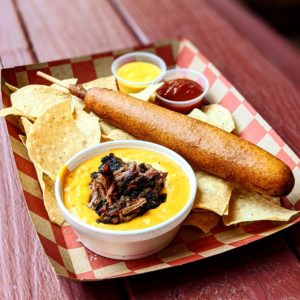 a foot long corn dog with chips and relishes is served in a basket for fair fare on the square