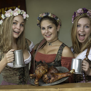 three women dressed for a renaissance faire in the square pose with turkey legs and steins.