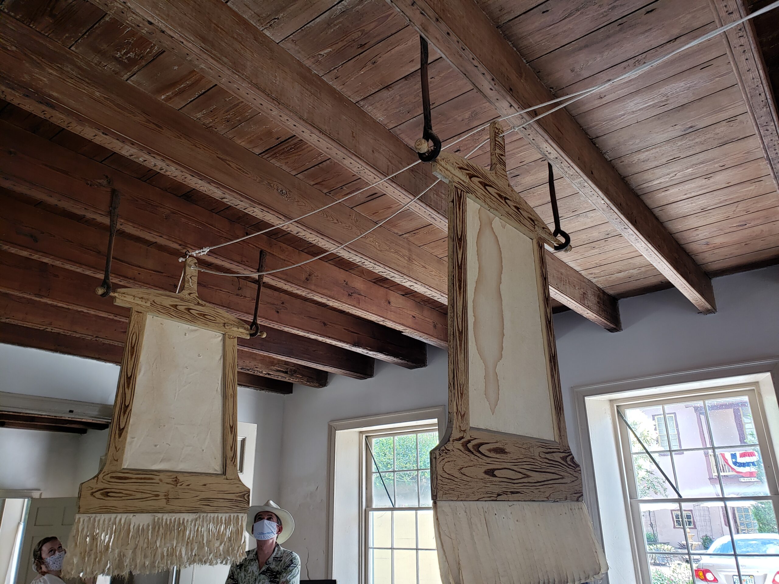 These ceiling fans installed over the table are made from an off white linen (?) and have fringe at the bottom. They are huge rectangles, upright.